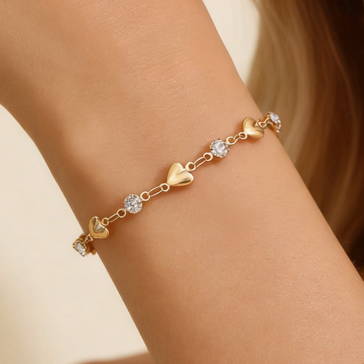 Venus Heart Bracelet worn on the wrist — gold hearts and clear stones on a fine chain